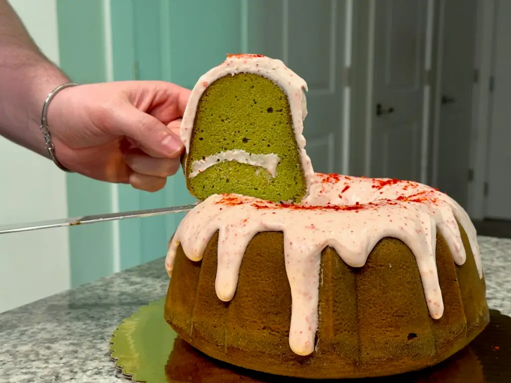a person holding a slice of matcha cake with strawberry icing