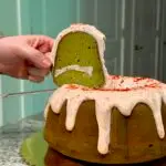 a person holding a slice of matcha cake with strawberry icing